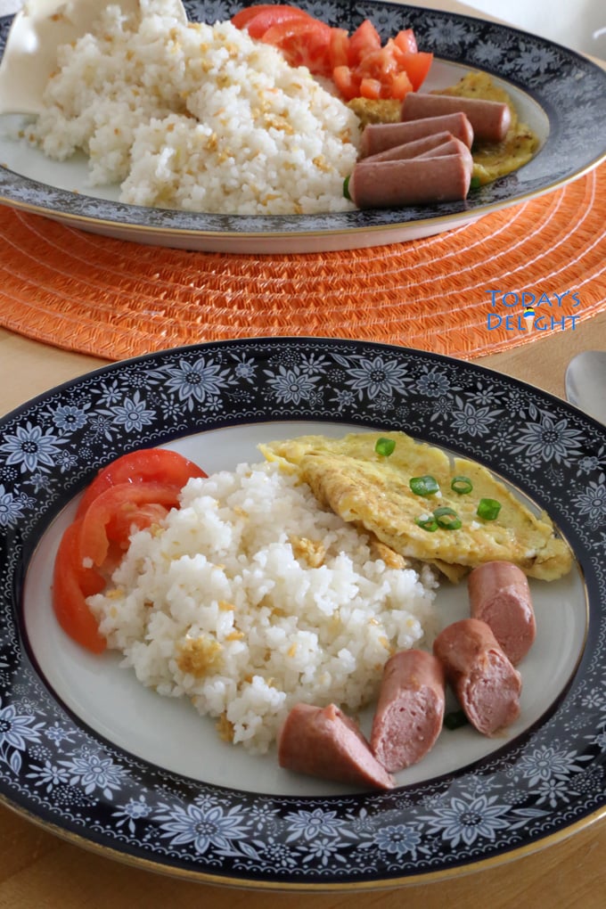 Sinangag or garlic fried rice on a plate with fresh tomato, egg and sausage.