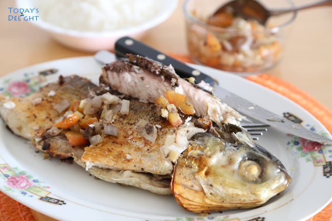Grilled milkfish with head stuffed with tomato and onion on a plate and side of rice and stuffing.