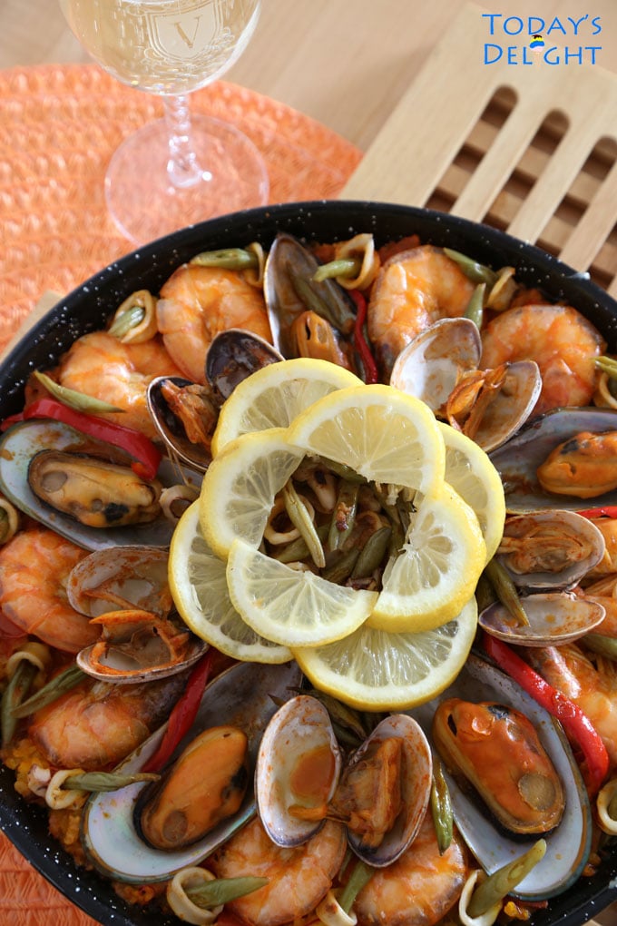 Seafood paella cooked on a paellera topped with mussels, manila clams, sliced squid, green beans and slices of lemon in the middle.