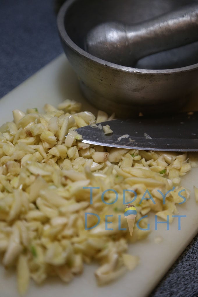 Peeled garlic on a cutting board with a knife and a pestle and mortar on the side.