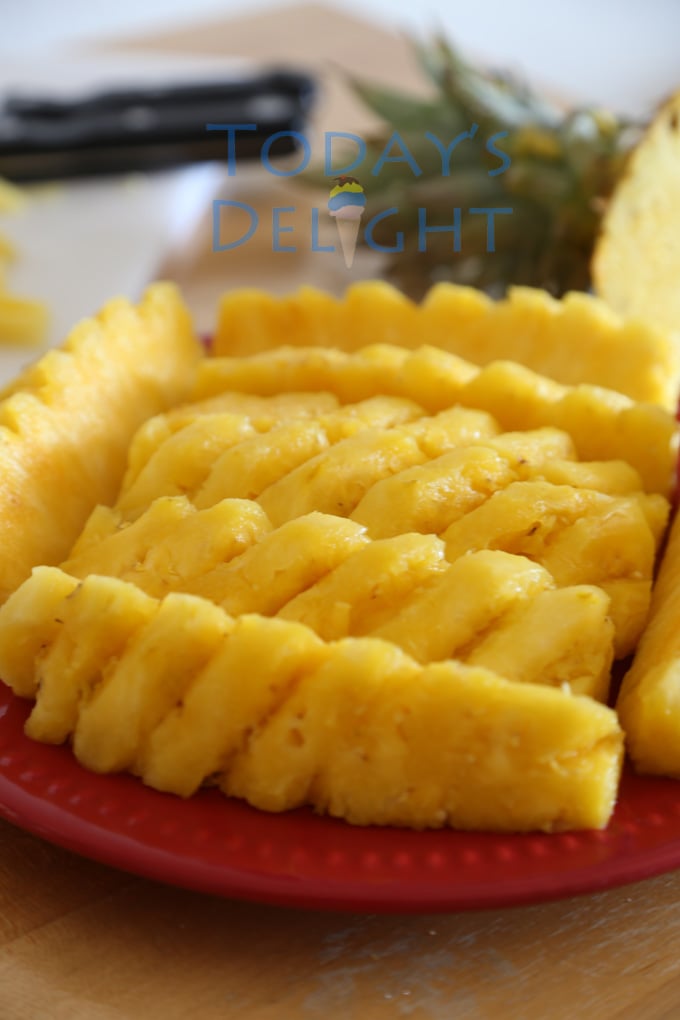 Peeled and sliced pineapples on a red plate. A knife and the top of the pineapple on the table too.