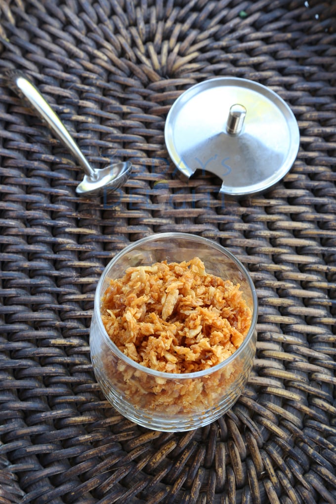 Toasted garlic in a glass cup with a small spoon and cover on a wooden tray.