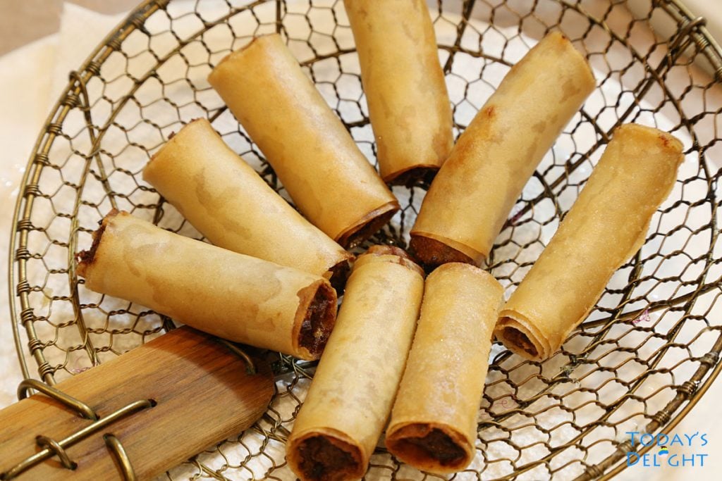 8 Lumpiang Shanghai (Filipino spring rolls) on a bamboo spider strainer.