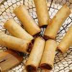 8 Lumpiang Shanghai (Filipino spring rolls) on a bamboo spider strainer.