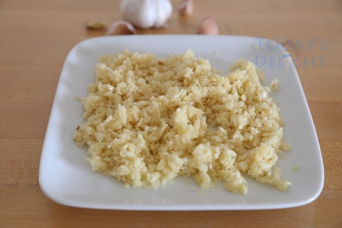 Blended or minced garlic on a plate and more garlic cloves on the table.