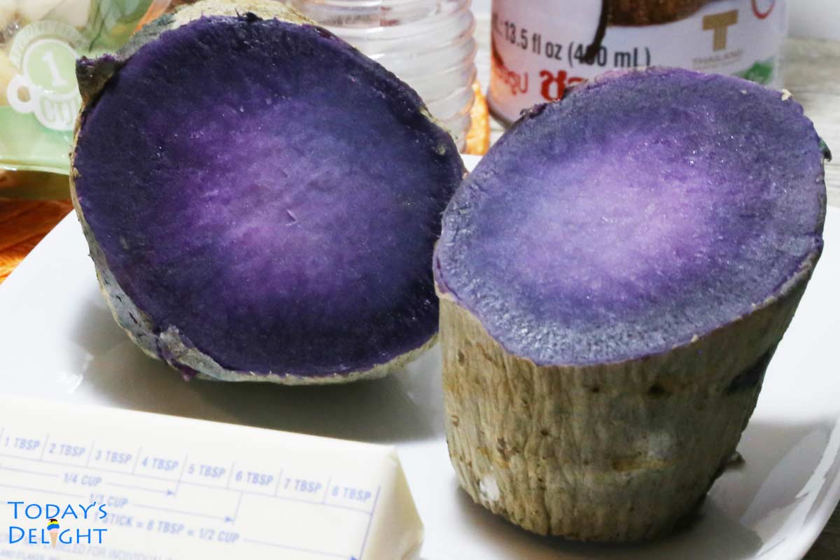 Cooked Okinawan sweet potato cut in half, butter, coconut milk in can and sugar on the table.