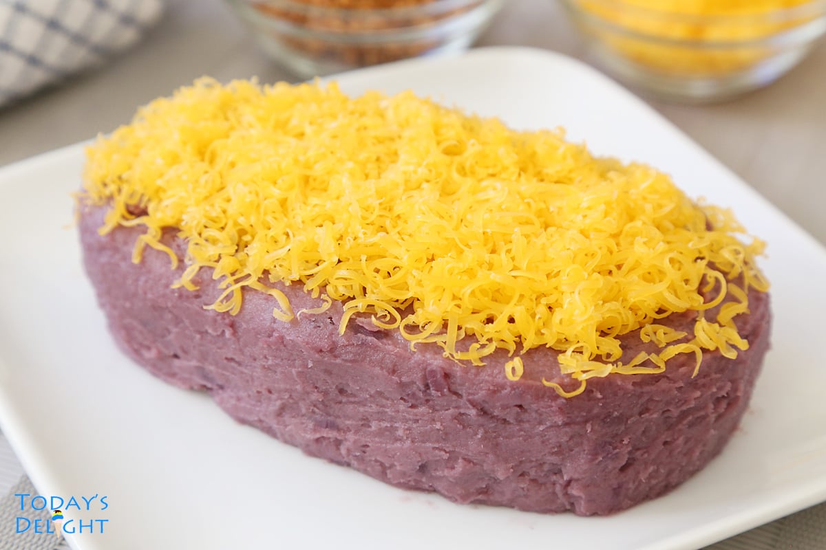 Purple yam jam topped with grated cheese known as ube halaya on a plate and a side of coconut curd and more grated cheese and both are in small bowls.