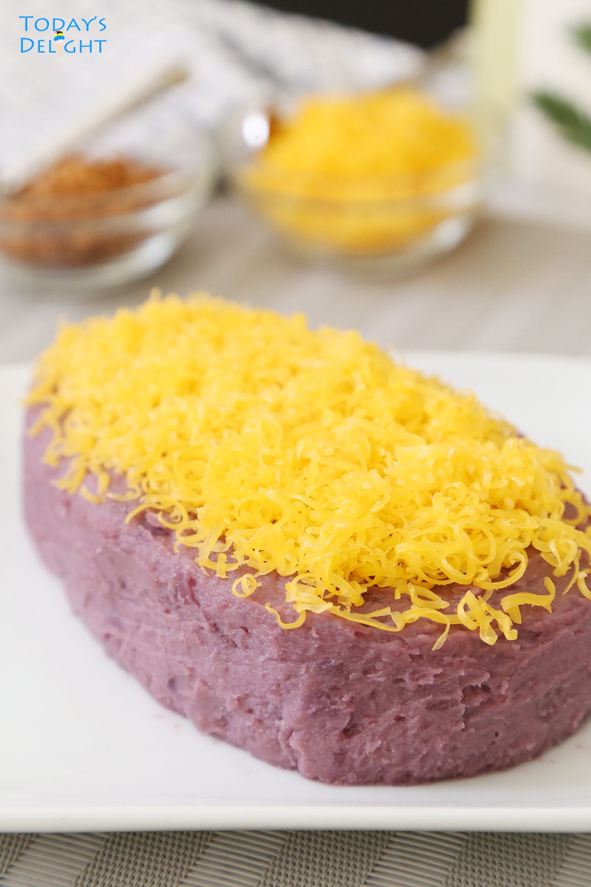 Purple yam jam topped with grated cheese known as ube halaya on a plate and a side of coconut curd and more grated cheese and both are in small bowls.