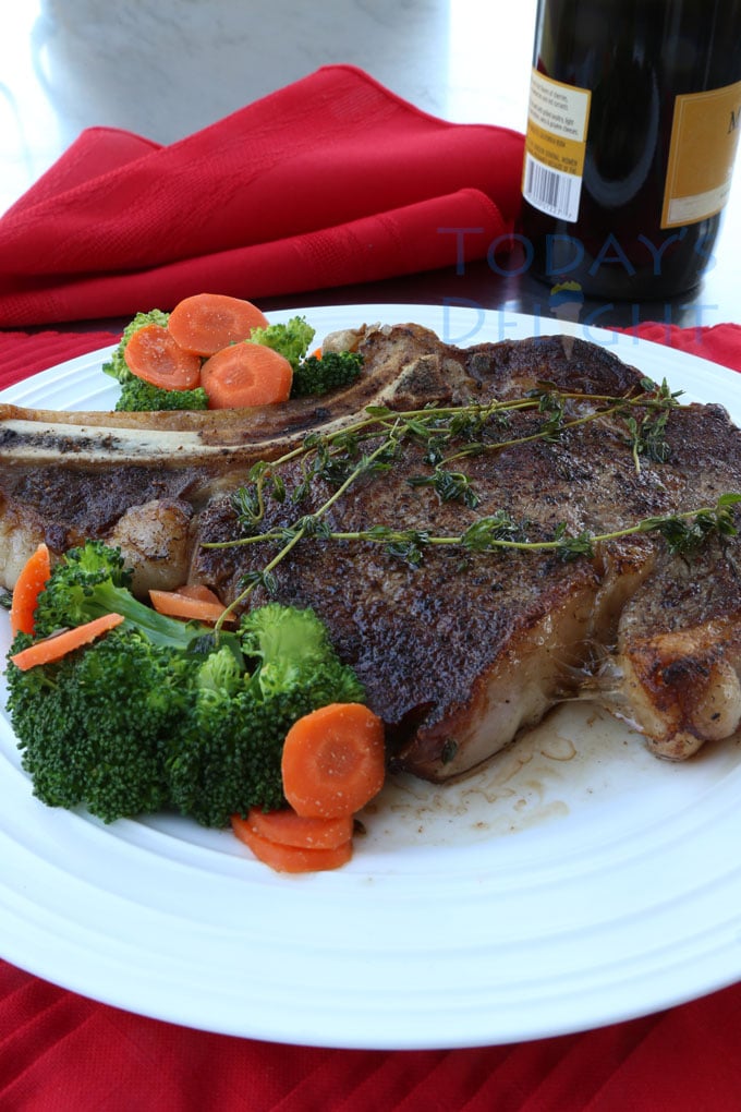 Pan fried ribeye steak with thyme on a plate with carrots and broccoli.