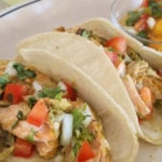 Two salmon tacos with mango salsa and lime wedges.