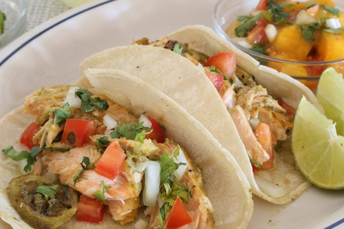 Two salmon tacos with mango salsa and lime wedges.