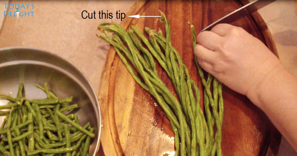 A bunch of sitaw (string beans) on cutting board with tip cut with a knife.