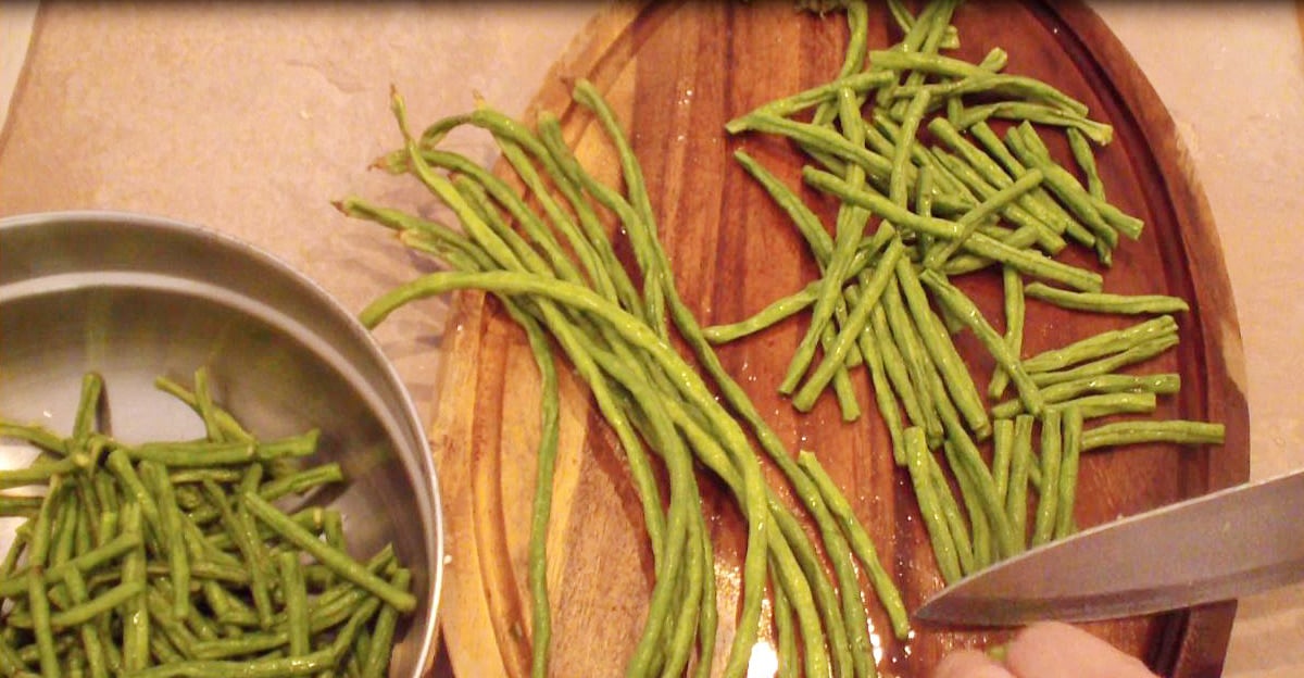 Cutting strings beans (sitaw) on cutting board with a knife.