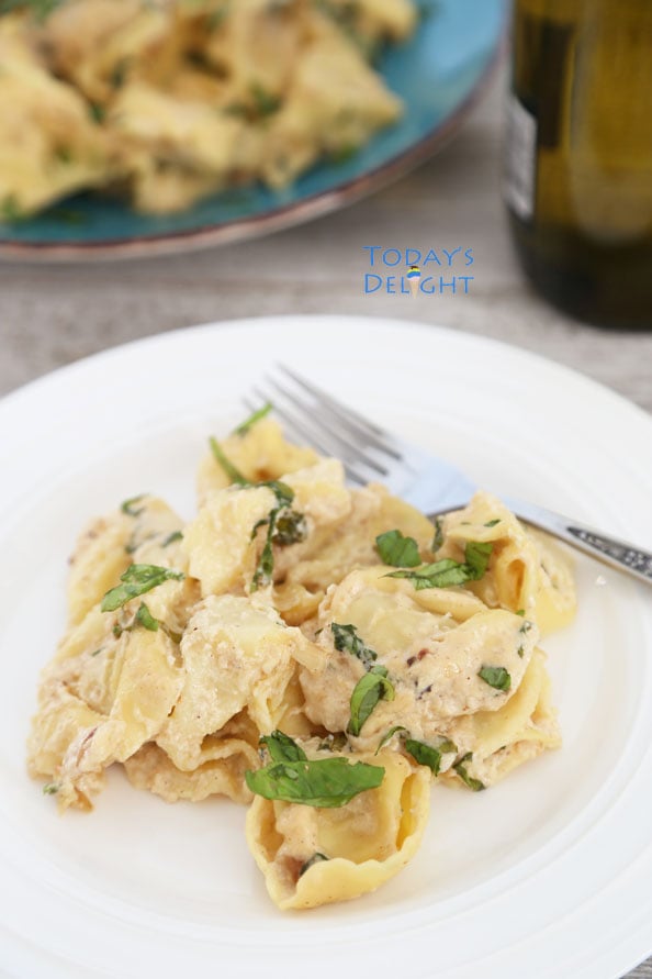 Two plates of cheese tortellini with fork and a bottle of wine.
