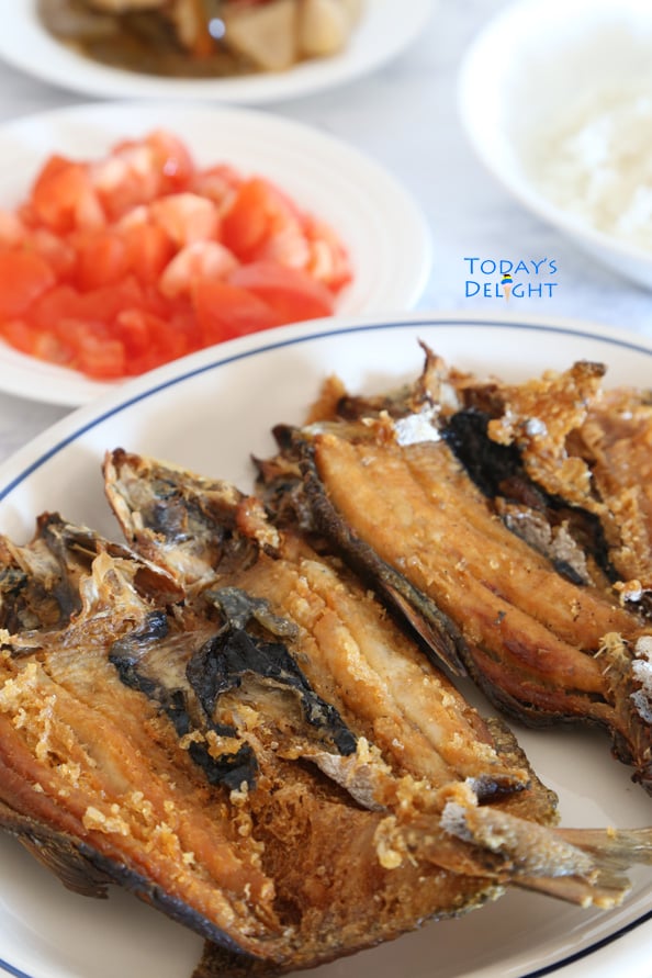 Two fried bangus (milkfish) on a platter, a side of chopped tomatoes, pickled vegetables and rice.