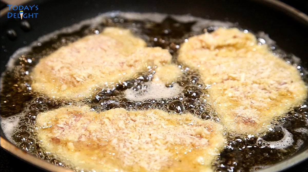 Three breaded pork schnitzel are fried in oil on a non-stick pan.