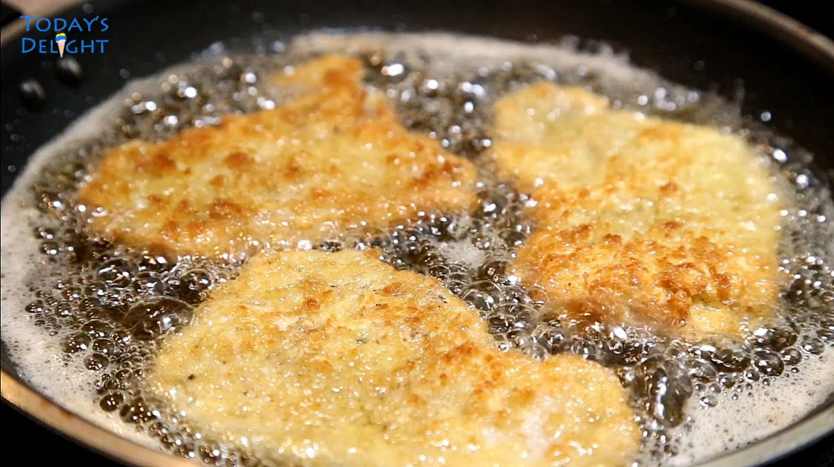 Three breaded pork schnitzel are fried in oil on a non-stick pan until light brown.