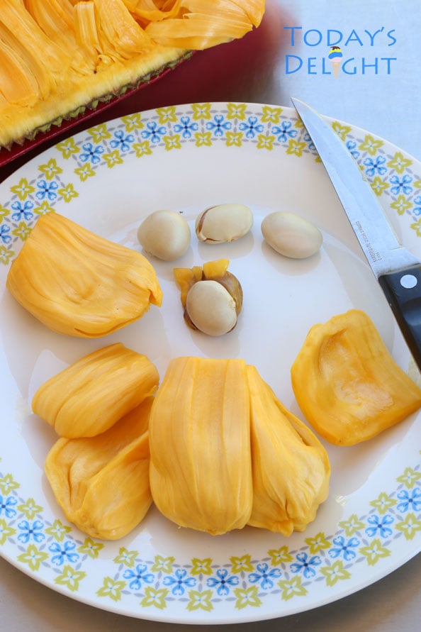 Pieces of jackfruit with seeds removed with a knife on a plate and half of jackfruit on the side.
