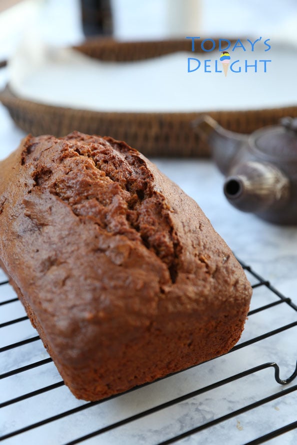 Baked pumpkin spice bread cooling on a rack. A wooden tray and tea warmer on the table.
