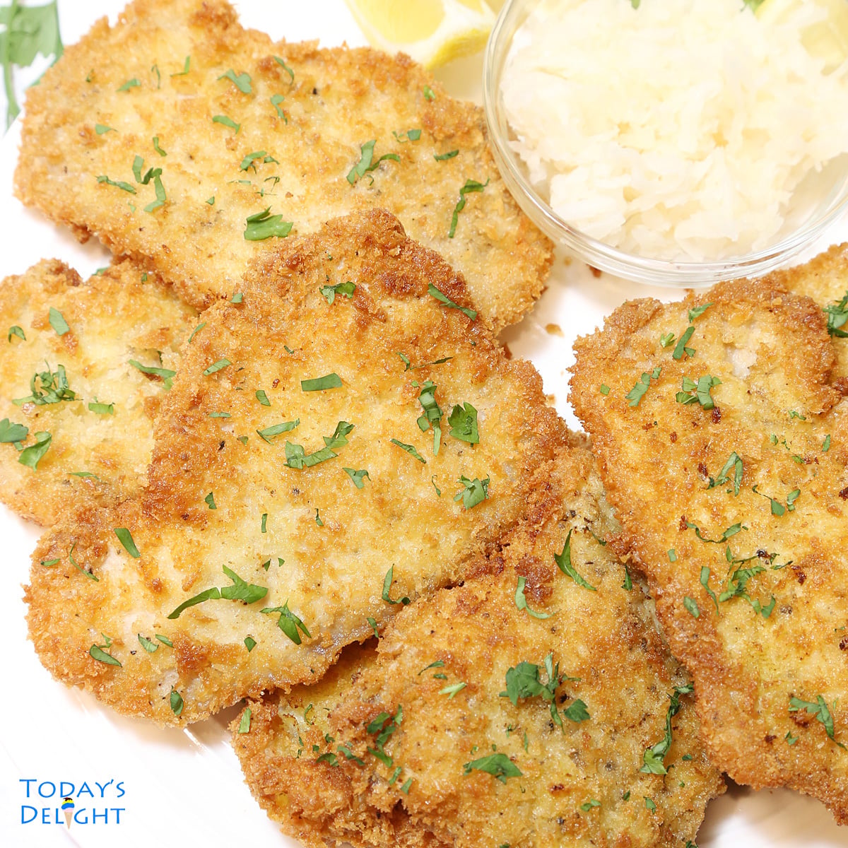Pieces of pork schnitzel on a platter garnished with parsley and a side of lemon wedges and sauerkraut.