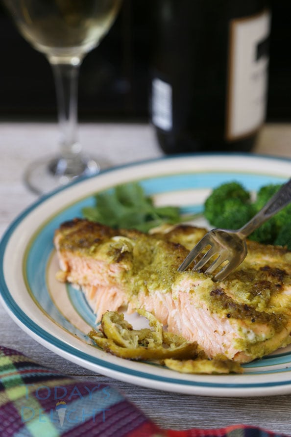 Salmon with lime, cilantro and jalapeno sauce on a plate with a piece of salmon on a fork and broccoli on the side. Wine glass and a bottle of wine in the background.