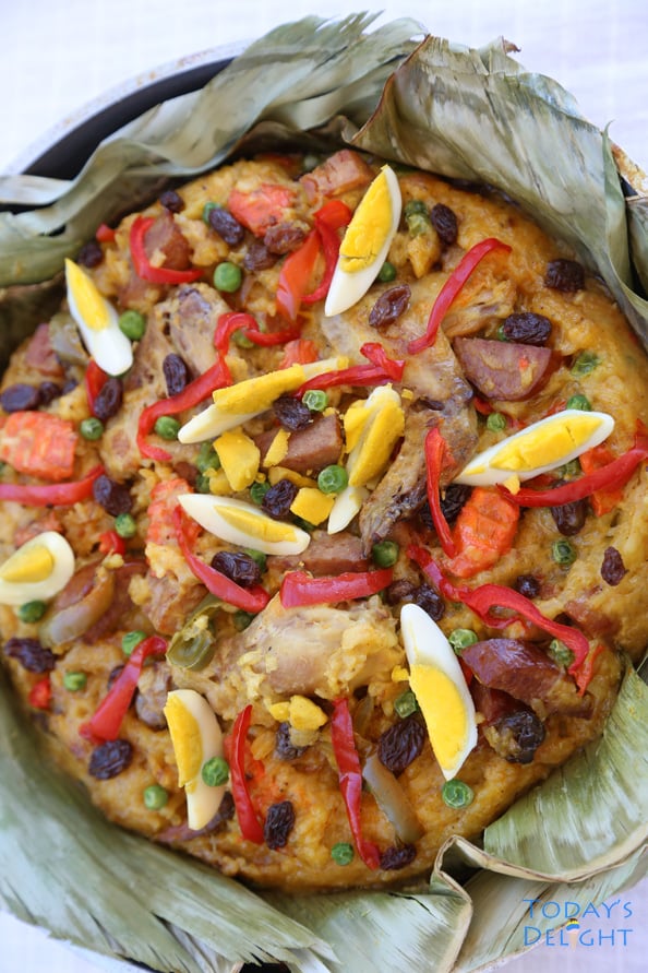 Bringhe (Philippines native paella) made of glutinous rice topped with meat, hard-boiled eggs, strips of red bell pepper, raisins and green peas on a pan lined with banana leaves.