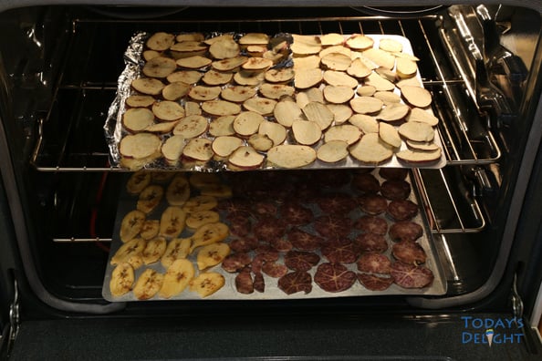 Two baking trays with banana chips, purple yam, and sweet potatoes seasoned with pumpkin spice in the oven.