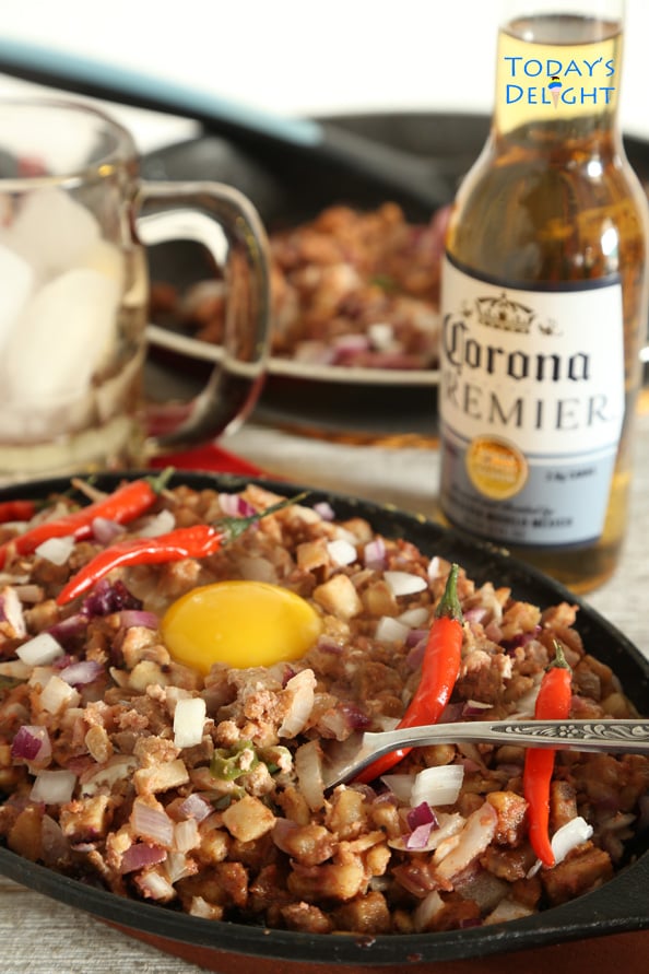 A serving of sisig (pork belly dish) on a hot plate, a beer bottle, a mug and dish in the pan.