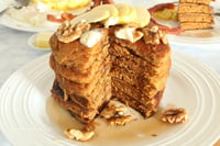 Sliced layers of Pumpkin Spice Pancake with syrup and topped with apple slices, walnuts.