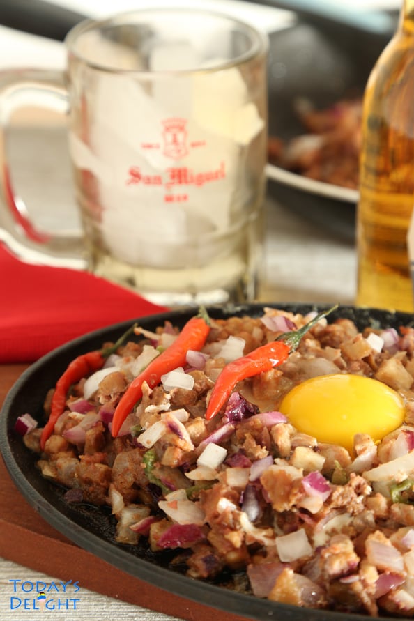 A serving of sisig (pork belly dish) on a hot plate, a beer bottle, a mug and dish in the pan.