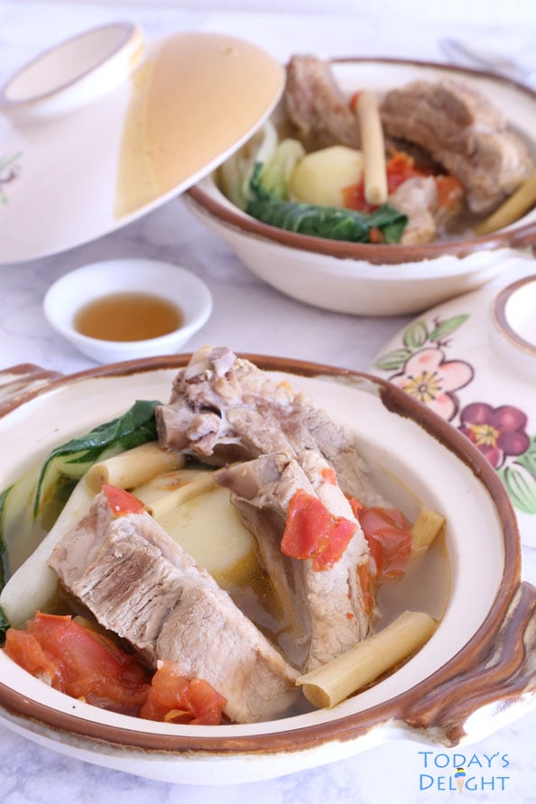 Two bowls of spareribs soup with tomato, potato, lemongrass and bokchoy; and, a side of fish sauce.
