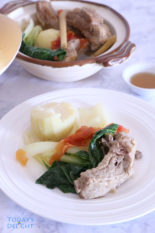 A bowl of spareribs soup with tomato, potato, lemongrass, and bokchoy, a plate with rice and the soup ingredients, and a side of fish sauce.