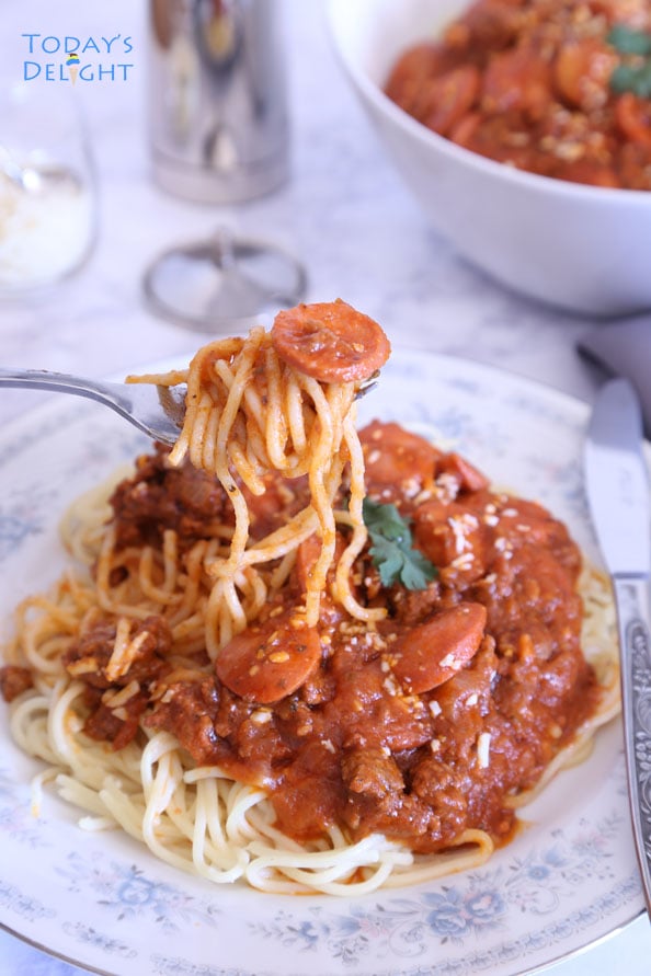 A plate of Filipino Spaghetti with meat sauce and hot dog and spaghetti noodles in a fork.
