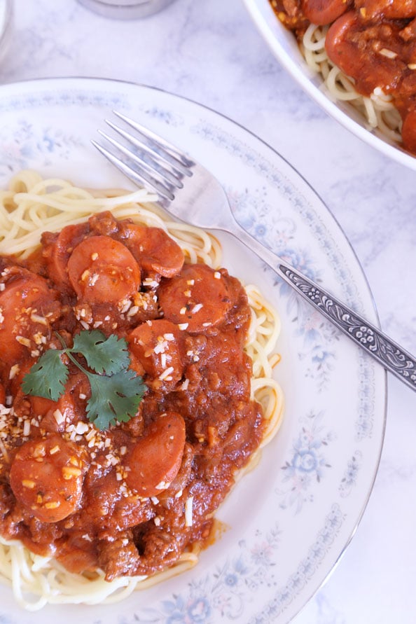 A plate of Filipino spaghetti in hot dog meat sauce garnished with parsley and parmesan cheese.