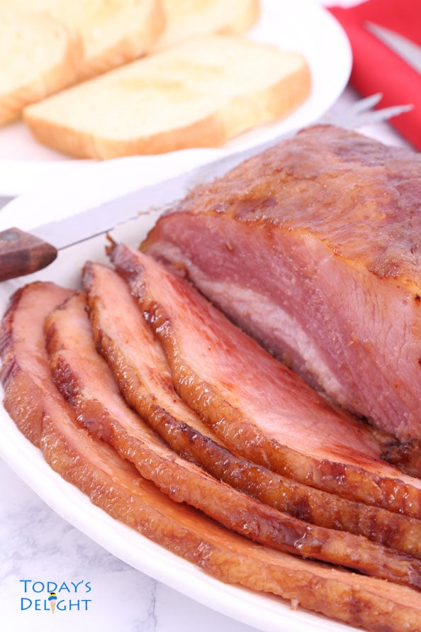 Sliced pineapple carver ham on a platter and a plate of bread.