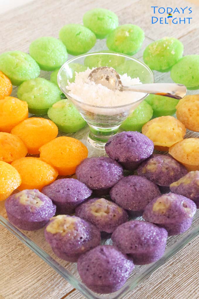 Colored rice cakes served on a glass platter and grated coconut servings with serving spoon in the middle of platter.