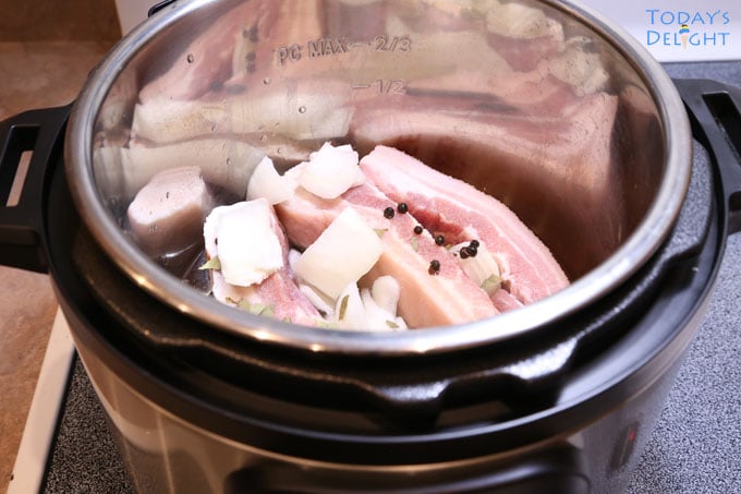 Slices of pork seasoned with whole black peppers, onion, and other seasonings in an instant pot.