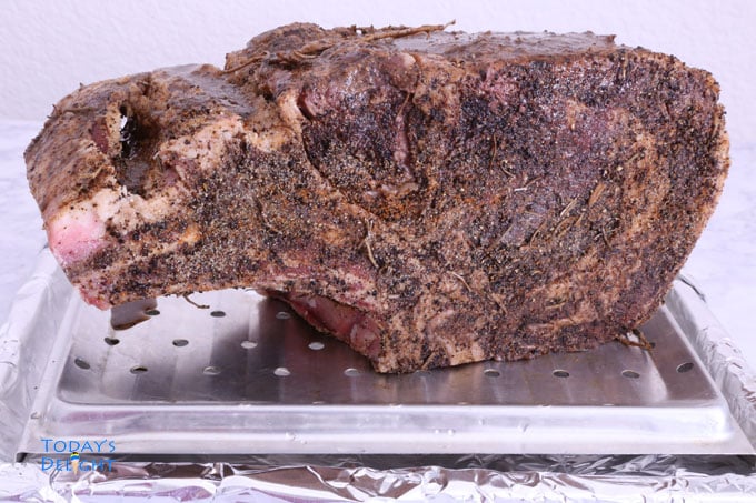 Seasoned bone-in rib eye roast on an oven tray.
