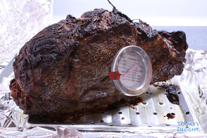 Seasoned standing bone-in rib eye roast with a thermometer and on an oven tray.