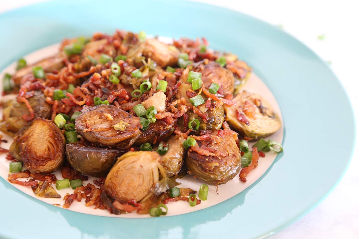 One serving of Brussel sprouts with bacon bits garnished with chopped green onions on a light blue plate.