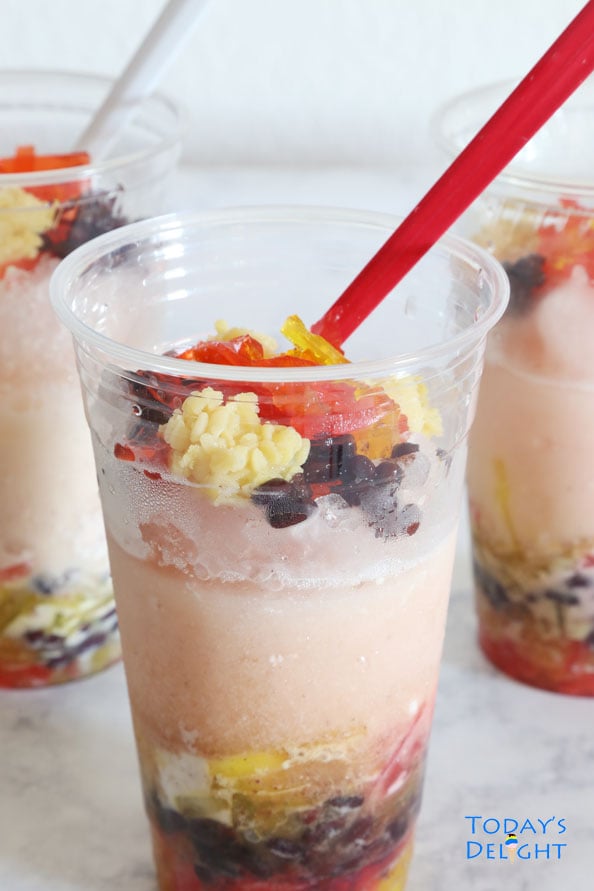 Three Asian desserts with mung beans, red beans, agar-agar, coconut milk, and shaved ice in plastic cups with red spoons.