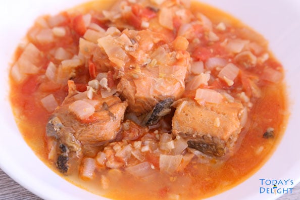 A can of salmon sautéed in onion, garlic, and tomatoes on a serving dish.