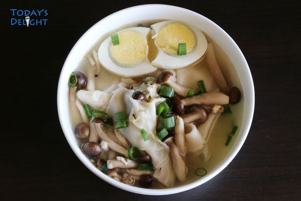 Wonton soup with beech brown mushrooms, sliced hard boiled egg, and greens onions in a soup bowl.