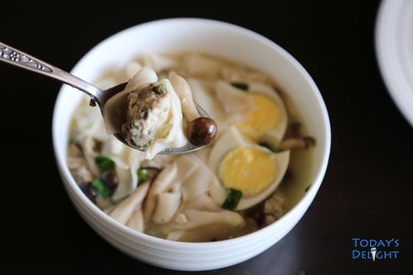 Wonton soup with beech brown mushrooms, sliced hard boiled egg, and greens onions in a soup bowl. Soup in the spoon.
