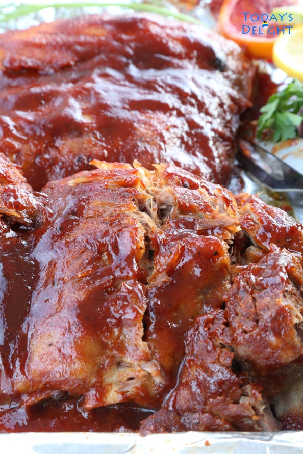 Baby back ribs on a tray with some fruits and hebs.
