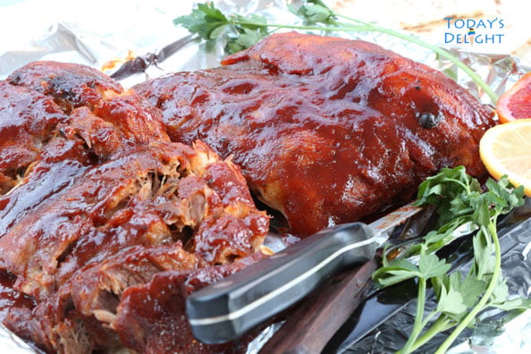 Baby back ribs with utensils, lemon and herbs on a tray.