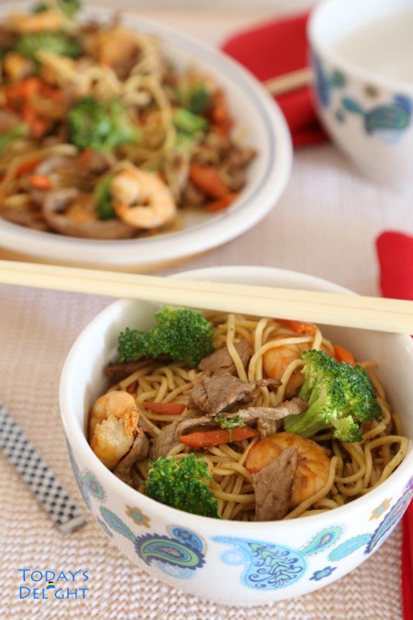Chinese Lo Mein noodles with pork, shrimp and vegetable in a serving platter and a bowl with chop stick.