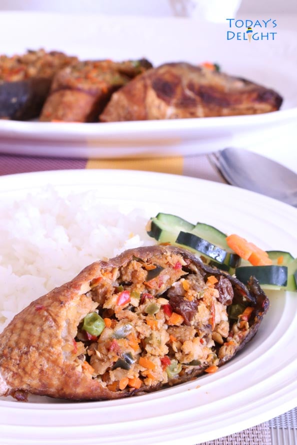 Rellenong bangus (stuffed milkfish) with cucumber, carrots, and white rice on a plate. In the background is the whole fish on a platter.