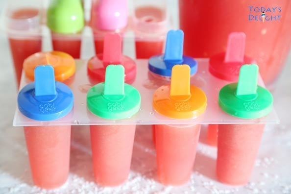 Sixteen watermelon popsicles that are still in the molds and a pitcher of the watermelon to make more popsicles.