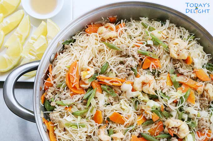 Pancit Bihon in skillet with lemon and fish sauce on the side.
